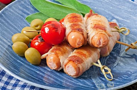 Gegrillte würstchen in speckstreifen mit tomaten und salbeiblättern