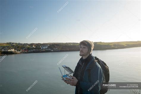 Male hiker operating drone near lake at countryside — summertime ...