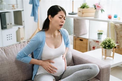 집에서 복통으로 고통받는 젊은 임신한 아시아 여성 배 아픈 아기가 몸 안에서 자라나는 불편함 한국의 미래 엄마 소파 소파에