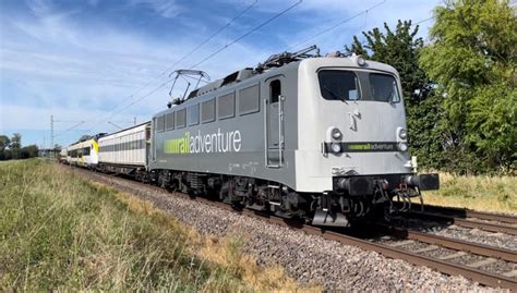 A Train Is Traveling Down The Tracks Near Some Grass And Trees On A