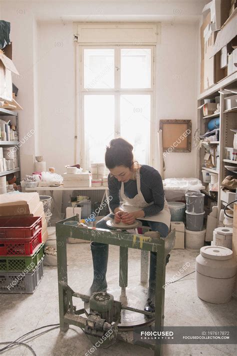 Caucasian woman is shaping pottery clay on a pottery wheel in a ceramic ...