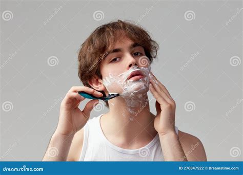 Portrait Of Young Man Shaving Face With Razor And Cream Posing Against