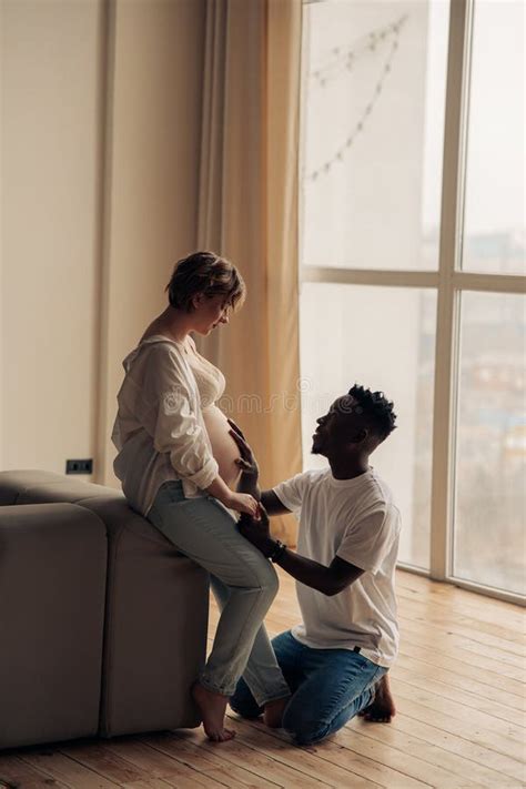 African Man Kneels Before Caucasian Pregnant Woman And Touches Her