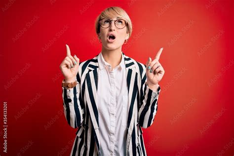 Blonde Business Woman With Short Hair Wearing Glasses And Striped Jacket Over Red Background