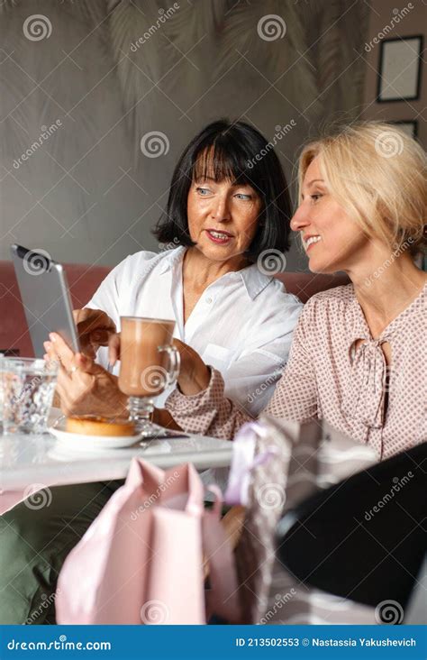 Two Mature Women Chatting And Using The Tablet Device While Having