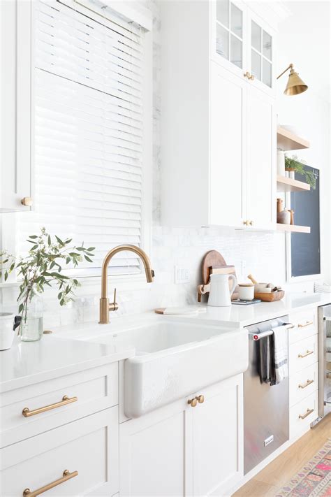 A Kitchen With White Cabinets And Gold Faucets An Area Rug On The Floor