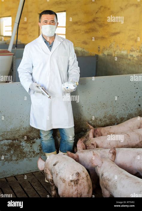 Man Veterinarian In Protective Clothing Holding Syringe And Glass