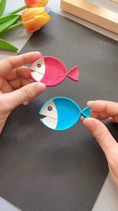 Two Hands Are Holding Small Paper Fish On A Table