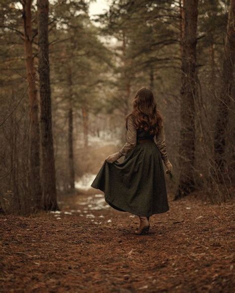 A Woman Is Walking Through The Woods In A Green Dress And Brown