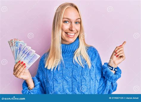 Jeune Fille Blonde Tenant Des Billets De Couronnes Suédoises Souriant Heureux Pointant Avec La