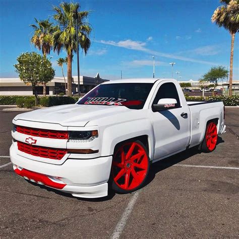 a white truck with red rims parked in a parking lot next to palm trees