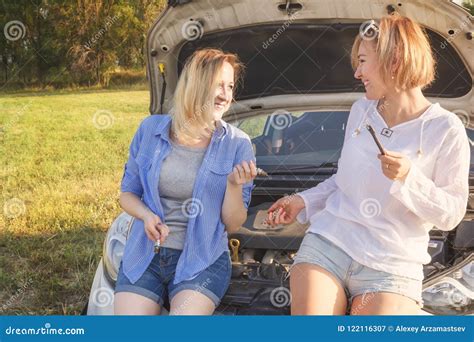 Two Beautiful Blonde Girls Are Having Fun Discussing Car Repairs On A Country Road In The Rays