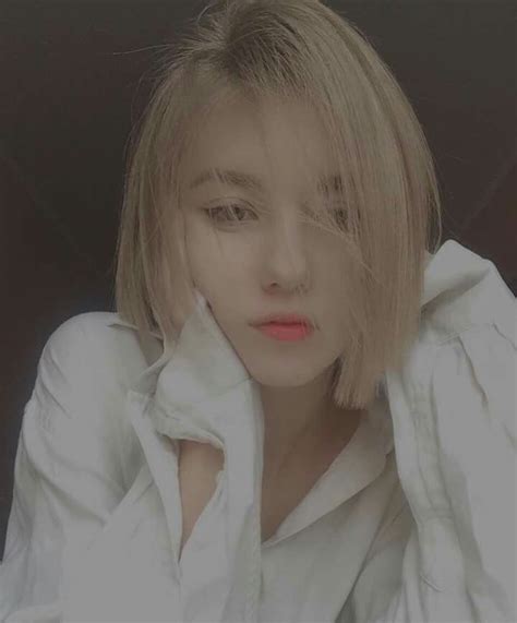 A Woman With Blonde Hair Wearing A White Shirt And Looking Off To The Side While Holding Her