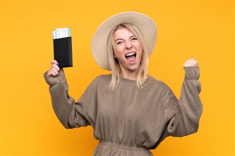 Junge blonde Frau über isolierte gelbe Wand glücklich im Urlaub mit Pass und Flugtickets