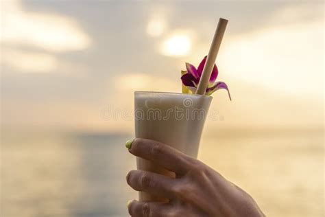 Female Hand Holds A Glass With A Pina Colada Cocktail On A Background