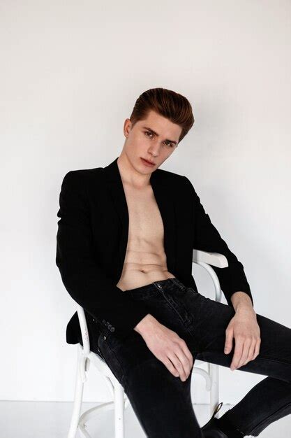 Premium Photo Fashionable Guy In A Black Blazer And Jeans With A Naked Torso Sits On A White