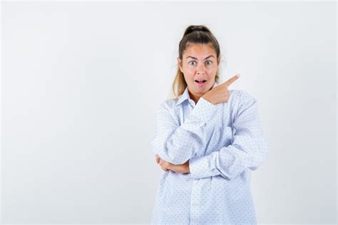 Mujer joven con camisa blanca apuntando a la derecha con el dedo índice