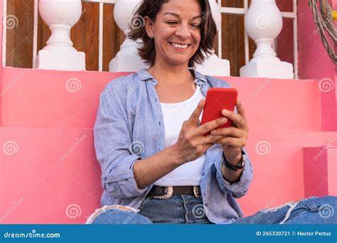 Mujer Latina Sentada En La Calle Con Las Piernas Cruzadas Y Sosteniendo Su Celular Imagen De