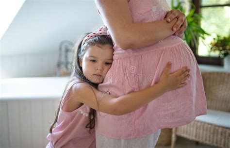 Portrait Of Pregnant Woman With Small Daughter Indoors At Home Hugging