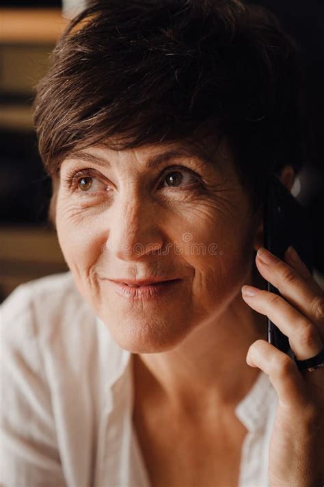 Smiling Mature Woman Talking On Cellphone While Sitting At Home Stock