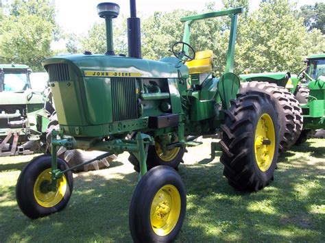 Two Large Green Tractors Parked Next To Each Other On A Lush Green