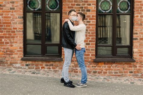 Pareja gay joven con máscara médica abrazándose en la ciudad Foto Premium