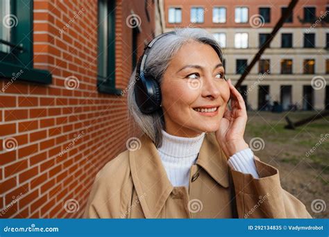 Mature Asian Woman Listening Music While Strolling On City Street Stock