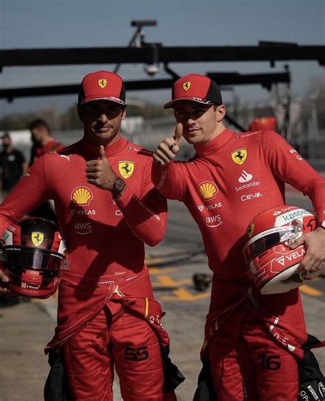 Two Men In Red Racing Suits Standing Next To Each Other