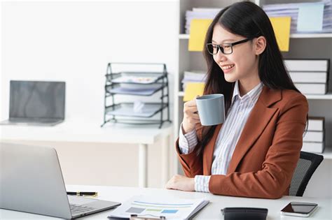 사무실에서 커피를 마시고 노트북을 사용하는 쾌활한 얼굴을 가진 젊은 사업가 책상에 앉아 컴퓨터에서 이메일을 확인합니다 현대적인