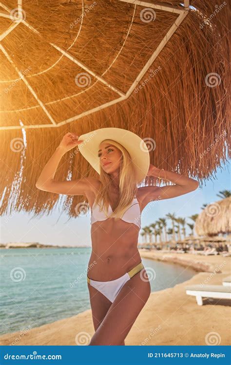 Woman Wearing Bikini Standing Under Straw Canopy Umbrella At The Beach