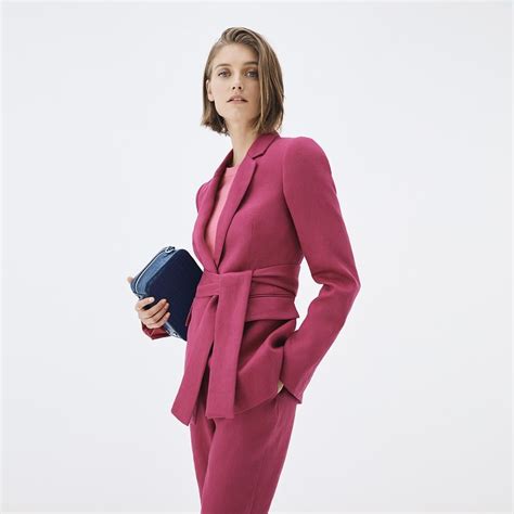 A Woman Wearing A Pink Suit And Holding A Blue Purse In Her Hand