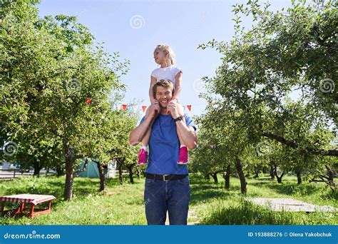 Happy Father Carrying Daughter On His Shoulders In Garden Stock Photo