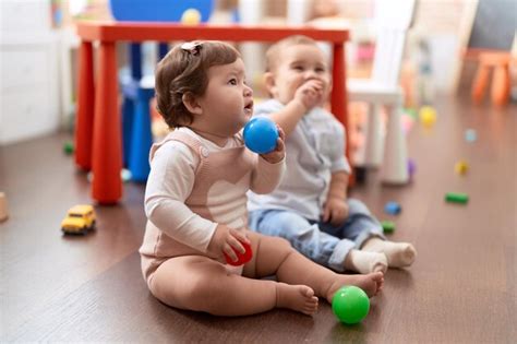 Dos niños pequeños jugando con pelotas sentados en el piso en el jardín