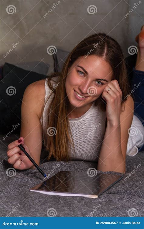 Smiling Woman Lying On Her Stomach In Bed With A Notebook Stock Image