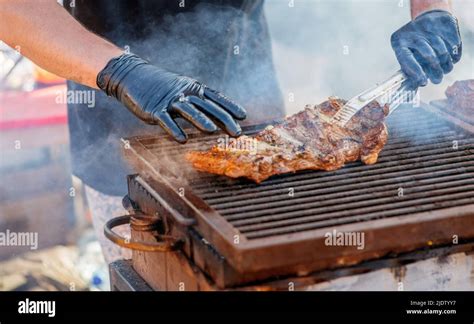 Barbecue Ribs Man In Gloves Flips Grilled Ribs On A Charcoal Grill