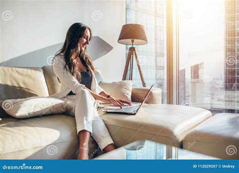 Elegant Young Female Business Woman Using A Laptop Sitting On A Sofa At