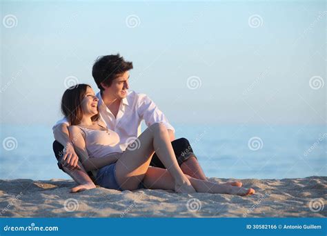 Couple Sitting And Laughing On The Sand Of The Beach At Sunset Stock