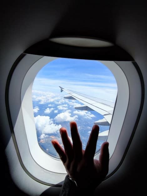 La mano de una persona está mirando por la ventana de un avión Foto