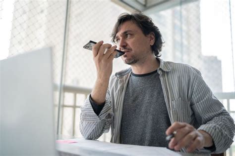 A Man Sitting At A Table With A Laptop And Cell Phone In His Hand While