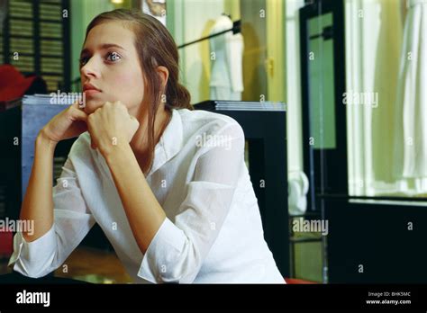 Young Woman Sitting With Hands Under Chin Looking Away In Thought