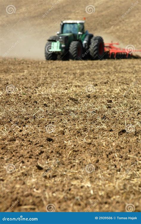 Tractor Ploughing Field With Blurry Farm In The Background Royalty Free
