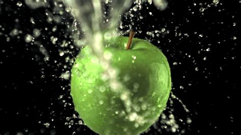 Super slow motion on the rotating apple drops water with splashes. On a ...