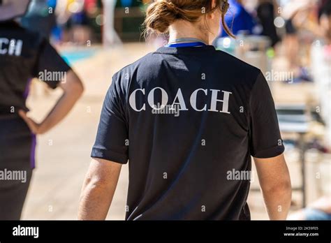 Back View Of Swimming Coaches Wearing Coach Shirt Working At An