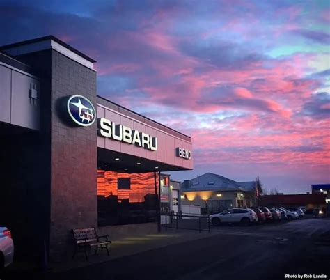 a subaru car dealership at dusk with the sun setting in the sky behind it