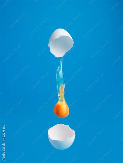 Egg Yolk Dripping Falling Between Cracked Eggshell On Vibrant Blue