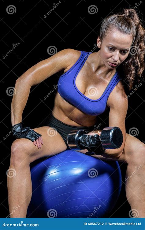 Thoughtful Woman Lifting Dumbbell While Sitting On Exercise Ball Stock