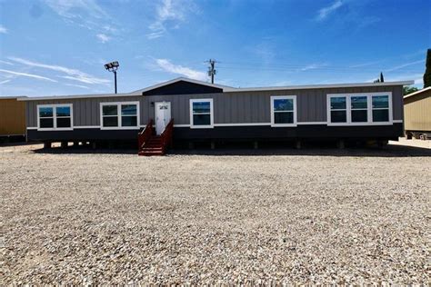 A Mobile Home Sits In The Middle Of A Gravel Lot With Stairs Leading Up