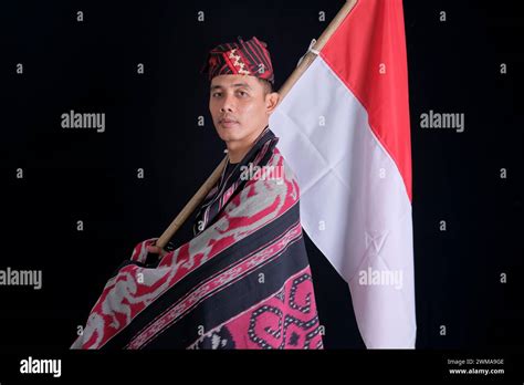 man wearing traditional woven clothes holding indonesian national flag