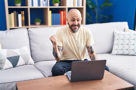 Hispanic Man With Tattoos Using Laptop At Home Screaming Proud