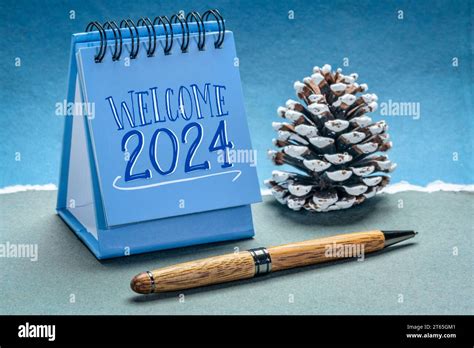 welcome 2024 in a spiral desktop calendar with a decorative frosty pine cone against handmade ...